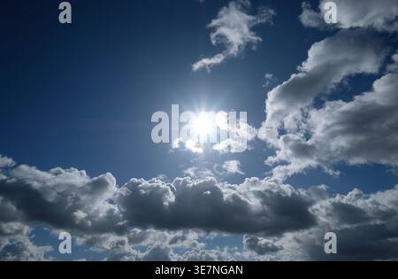 backlit sunburst behind clouds on blue sky background Stock Photo