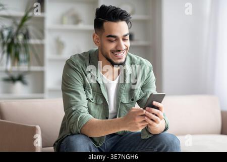 Arab man using smartphone sitting on sofa in living room at home Stock Photo