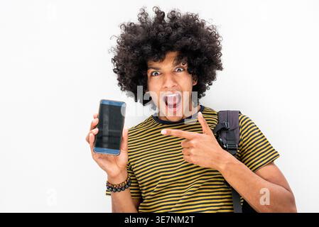 Surprised African American man holding and pointing to smartphone standing against wall Stock Photo