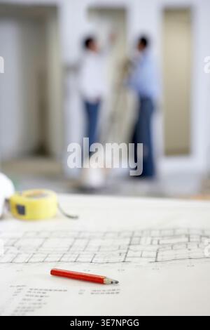 Chinese male architects talking to each other while standing near blueprint in building site Stock Photo