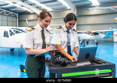 Middle Eastern female pilot using laptop standing beside her co-pilot in hangar Stock Photo