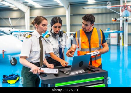 Middle Eastern female pilot with her team using laptop for airplane checkup in hangar Stock Photo
