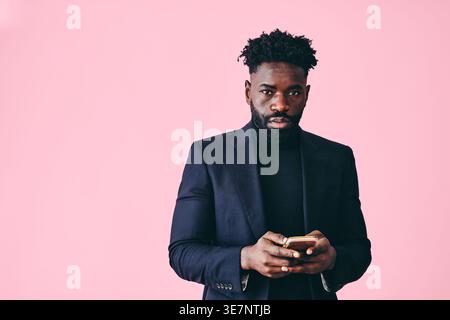 Black man with beard holding smartphone standing against pink background in studio Stock Photo