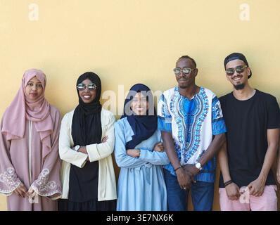 Smiling diverse group of friends standing together and leaning against yellow wall Stock Photo