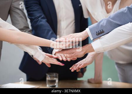 Diverse group of business people stacking hands standing together in meeting room Stock Photo
