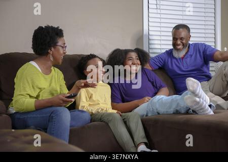 Cheerful Black family sitting together on couch and watching tv having fun in living room at home Stock Photo