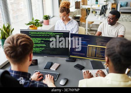 Diverse group of programmers working on computers sitting at  table in office Stock Photo