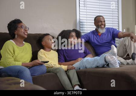 Cheerful Black family sitting together on couch and watching tv having fun in living room at home Stock Photo