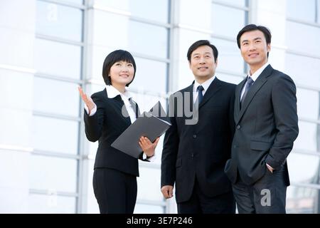 Chinese business woman discussing work to male colleagues standing near building in city Stock Photo