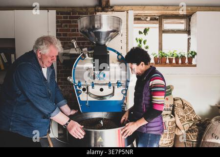 Hispanic woman and caucasian man standing next to coffee roasting machine indoors Stock Photo