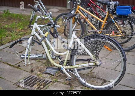 A close-up view of several bicycles parked and locked to a metal rack on a paved sidewalk in an urban residential area. In the foreground, a white Stock Photo