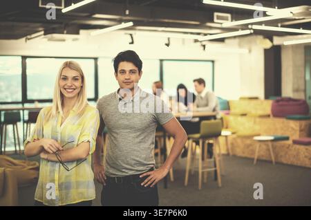 Mixed race businessman and caucasian business woman standing together near colleagues having a meeting in the office Stock Photo
