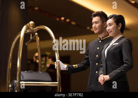Smiling Chinese male and female staff looking away while standing in hotel lobby Stock Photo