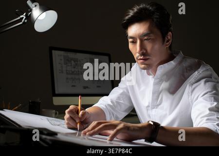 Chinese male architect working on construction plan sitting at table in office Stock Photo