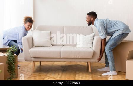 Tired Black couple lifting and moving sofa together after moving in new home Stock Photo