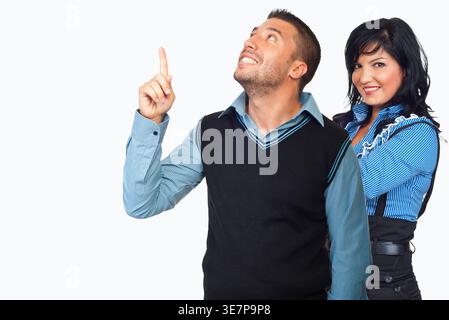 Man and woman stand against plain white background. Man points upward, smiling with hopeful expression. Woman stands beside him, smiling warmly at vie Stock Photo