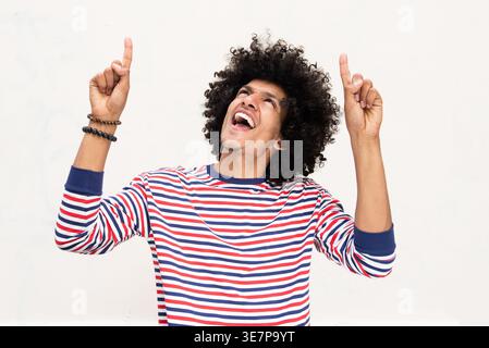 Smiling African American man pointing fingers up standing against white wall Stock Photo