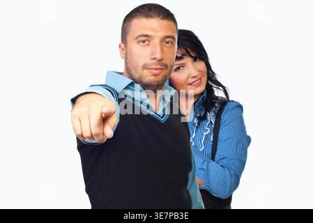 Man points directly at viewer with serious gaze. Woman smiles softly behind him, leaning slightly. Bright white background emphasizes their presence. Stock Photo