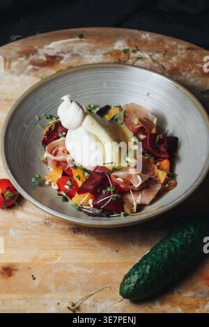 Gourmet Italian Burrata salad with fresh prosciutto ham slices cherry tomatoes beetroot and microgreens served in a ceramic bowl on a rustic wooden Stock Photo