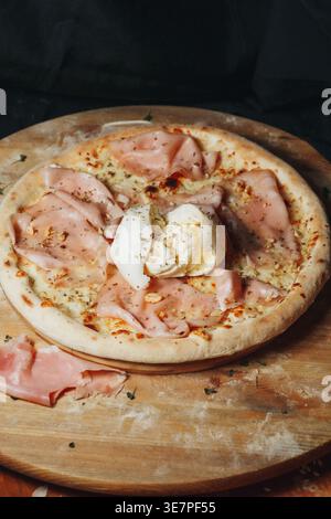 Traditional Italian pinsa romana topped with thin slices of savory mortadella ham a whole creamy burrata cheese and crushed pistachios on a wooden Stock Photo