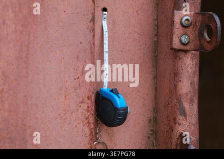 A tape measure is hanging on a rusty container door. This tool is used to measure and check dimensions for battery storage within a power grid system. Stock Photo