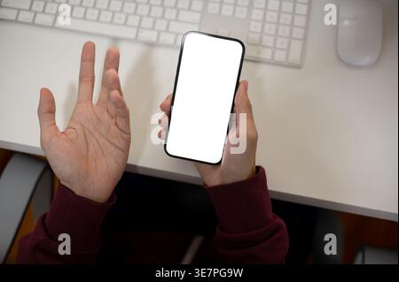 Man wearing maroon hoodie using smartphone while sitting at table in office Stock Photo