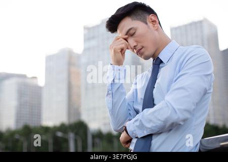 Chinese businessman having headache standing on bridge in city Stock Photo