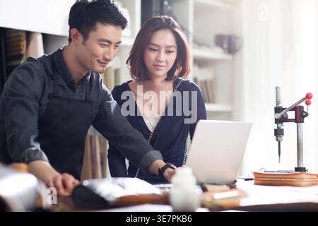 Chinese craftsman working on laptop while talking to female customer in shop Stock Photo