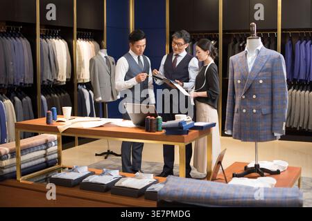 Chinese male and female fashion designers standing and working together in formal suits shop Stock Photo