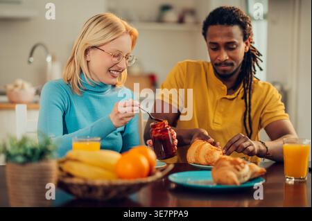 Serious Mixed race man with locks eating breakfast with caucasian girlfriend holding jam sitting at table at home Stock Photo