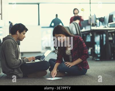 Mixed race man and caucasian female workmate working together sitting on floor in office Stock Photo