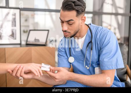 Arab male caregiver using pulse oximeter on patient index finger while sitting at home Stock Photo