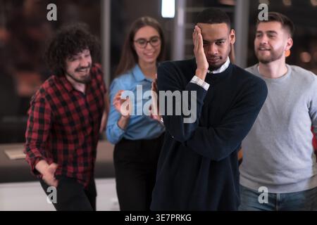 Black male with closed eyes and hand on face having fun with workmates playing game during break in office Stock Photo
