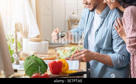 Cropped shot of young arab family preparing vegetable salad in kitchen together, unrecognizable middle eastern spouses enjoying cooking healthy foo... Stock Photo