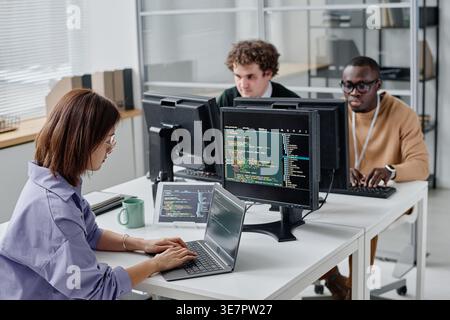 Group of diverse developers sitting at desk writing codes for new computer program in IT office Stock Photo