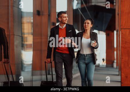 Smiling Hispanic business woman and caucasian businessman with luggage having coffee break from work walking on city street during daytime Stock Photo