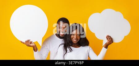 Black couple holding empty speech bubbles while standing against yellow background Stock Photo