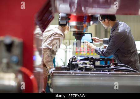 Chinese male engineers checking machine using tablet standing in factory Stock Photo