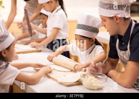 Chinese children learning how to cook with caucasian male teacher in school Stock Photo