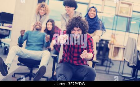 multiethnics startup business team of software developers having fun while racing on office chairs,excited Diverse employees laughing enjoying funn... Stock Photo