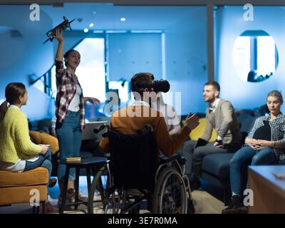 Diverse group of business people with disabled caucasian businessman using VR goggles and drone assistance simulation while having a meeting in the... Stock Photo