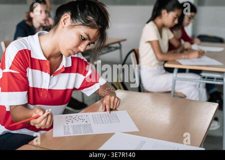 Asian female student and classmates sitting at desk taking exam in classroom Stock Photo