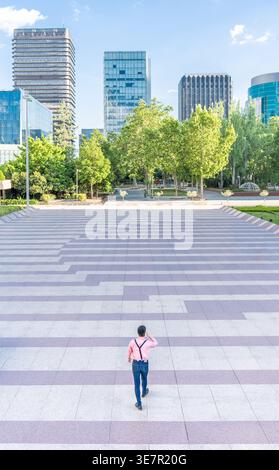 Asian man walking through an urban square in city on sunny day Stock Photo