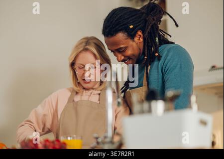 Smiling Mixed race man with locks and caucasian girlfriend preparing healthy food standing together at table with vegetables in kitchen at home Stock Photo