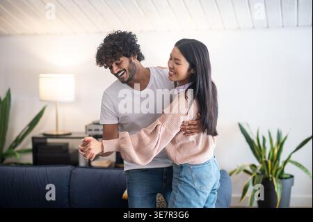 Cheerful Asian couple dancing together at home Stock Photo