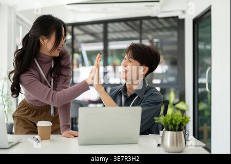 Asian male and female office workers giving high five to each other in office Stock Photo