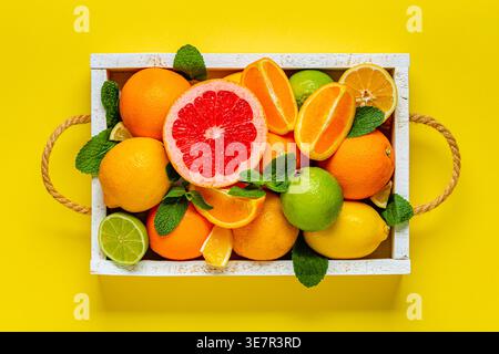 Fresh citrus fruits with leaves: lemons, oranges, mandarins, grapefruit, lime in wooden box, top view. Stock Photo