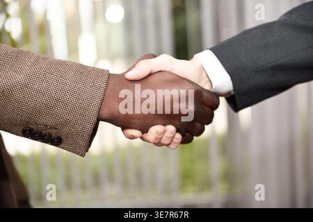 Black and caucasian businessmen wearing suits shaking hands while standing in office Stock Photo