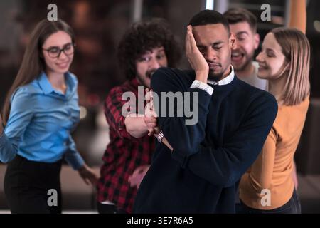 Black male with closed eyes and hand on face having fun with workmates playing game during break in office Stock Photo