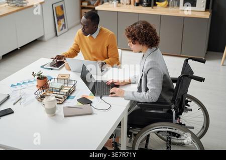Black man working with disabled caucasian female colleague using laptop sitting at table in office Stock Photo
